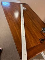 Full view of white wooden board with twelve hooks lying on a wooden table.