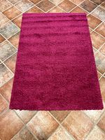 Top view of pink rectangular shag rug laid on tiled floor, showing texture and color.