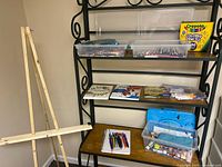 Photo showing wooden easel, shelves with clear containers holding colored pencils, a box of Crayola colored pencils, and art books on shelves.