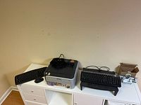 Office electronics bundle on white shelving includes Brother HL-2170W laser printer, Logitech wireless keyboard, and Logitech wireless mouse.