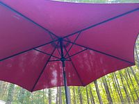 View of the opened umbrella showing the chili red fabric and black support ribs and pole.