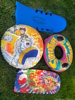 Three outdoor toys on grass: blue sled, colorful inflatable SUPERTUBE snow tube, and a round snow tube with warrior and polar bear graphic.