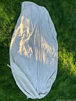 White oval outdoor table cover laid out on grass showing its shape and fabric texture.
