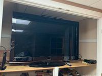 Samsung 52-inch TV positioned on wooden surface, showing entire front with stand and remote placed nearby.