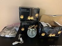 Six boxed solar glass decoration lights placed on a black surface, one removed from box showing glass globe and jute handle.