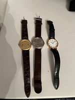 Photo of three men's wristwatches laid flat showing full leather straps and watch faces.
