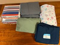 Top-down view of six folded twin sheet sets and one navy blue duvet cover with sham on a wooden surface.