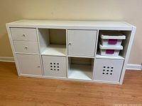 Front view of white wooden storage cabinet showing drawers, cabinet doors, cubbies, and two fabric bins along with two small plastic storage bins on the top right shelf