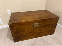 Closed wooden storage chest showing medium brown stain and brass hardware on corners and lid.
