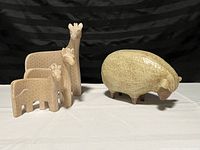 Photo showing one carved sheep figurine and three nesting giraffe figurines made of wood or similar material with textured detailing.