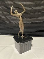Photo showing front and side view of the bronzed female dancer statue on black square base and gray pedestal.