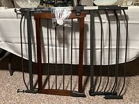 Photo of a black metal and dark brown wood framed pressure mounted safety gate with installation hardware attached in a plastic bag.