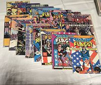 Photo showing a collection of American Flagg comic book issues laid out on a surface, arranged in a grid format. The collection includes issues 1 through 16 from First Comics.