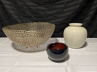 Photo of three home decor items: a large golden metal open-weave bowl, a small white ceramic planter, and a red and black glass bowl.