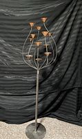 Full view of the tall iron and copper tea light holder showing the sculptural branches with copper cups against a black backdrop.
