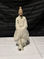 Front view of porcelain oriental man statue in traditional attire with crackled glaze, seated pose, 14 inches tall.