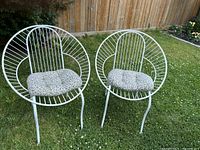 Photo showing two white metal wire frame patio chairs with round backs and leopard print cushions set on green grass outside.