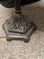 Close up of the metal base showing ornate scrollwork cutouts and four-footed structure on carpet.