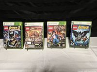 Four Xbox 360 Lego video game cases shown upright. Titles are 'Lego Batman 2: DC Super Heroes', 'Lego Indiana Jones', 'Lego Harry Potter', and 'Lego Batman'. Cases display cover art and Xbox 360 labels.