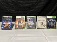 Five Xbox 360 game cases arranged side by side on a white surface with a dark background. Titles visible: Fable The Journey, Fable II, Sacred 2, Oblivion, Diablo III.