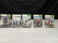Photo showing five Xbox 360 game cases lined up: Dishonored, Assassin's Creed II Platinum Hits, Assassin's Creed IV Black Flag, Far Cry 4, and Far Cry 3.