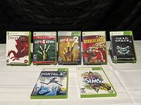 Photo showing 8 Xbox 360 game cases lined up on a white surface, displaying front cover art and titles.