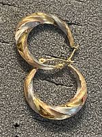 Top view of the pair of tri-colored 10K gold hoop earrings on a textured dark background.