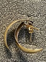 Photo showing the pair of medium-sized 14K gold hoop earrings lying on textured surface, with visible butterfly back posts and curved hoop shape.