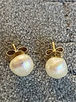 Pair of stud earrings featuring freshwater pearls and 14k gold posts with butterfly push-back closures on grey fabric.