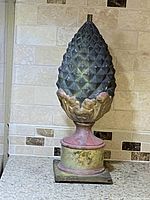 Full view of the vintage cast iron pineapple finial showing its size and overall colors against a tile backsplash.