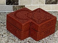 Full view of the red cinnabar lacquer box with carved floral and geometric patterns on an X-shaped body.