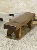 Angled view showing the overall shape and condition of the pine bench/stool. Visible morticed joints on the thick legs and wood grain texture.