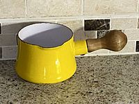 Yellow enamel butter warmer with white interior and wooden knob-style handle, displayed on countertop.