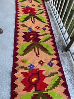 Long view of handwoven wool runner rug showing large floral geometric patterns with burgundy, green, and beige colors.
