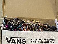 Box filled with assorted mixed jewelry including bracelets, bangles, necklaces, and earrings in various colors and materials.