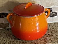 Orange ceramic bean pot with lid shown upright on kitchen counter.