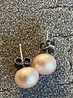 Pair of light peach pearl stud earrings on a textured surface, showing post and butterfly backing