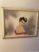 Framed portrait painting of a glamorous woman with short dark hair and red lips on a muted background.