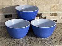 Three Pyrex blue mixing bowls stacked and arranged on countertop. Blue exterior, white interior, model 401, each approx 1.5 pt capacity.