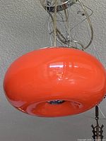 Side view showing the orange glass shade and chrome top with bundled suspension wires