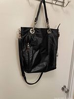Front view of black leather Rudsak bag hanging; shows zippered pocket and crossbody strap.