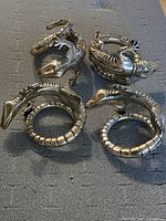 Four lizard-shaped napkin rings arranged on a dark fabric background showing front and side views.