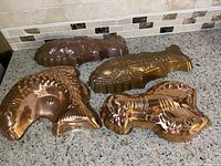 Four copper molds placed on countertop: three fish shapes, one lobster shape, showing size and detailed texture.