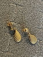 Both earrings lying on gray textured surface showing ribbed teardrop shape