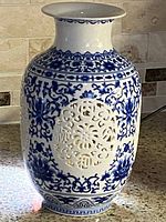 Front and side angle of the white and blue porcelain vase showing floral patterns and lattice cutout with Asian characters.