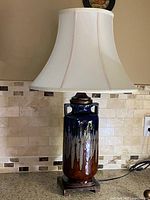 Front view of vintage ceramic table lamp with blue to brown glaze and white bell shade on ceramic and wood base