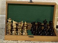 Opened folding wooden chess board with green felt lining and two sets of chess pieces (light and dark wood) arranged inside.