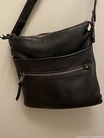 Front view of black leather crossbody bag with zippered pocket and adjustable strap.
