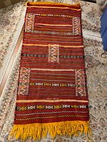 Full view of the rectangular handwoven wool rug laid out showing the colorful geometric and striped design with yellow fringe.
