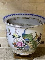 Front angle view of large vintage Asian ceramic planter showing peacock and floral design with multicolor accents and wear on interior rim.